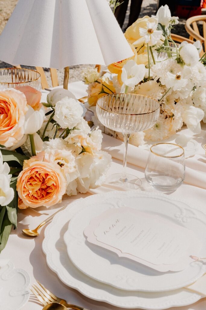 Decorated wedding table with peach-colored roses, table lamp, and crystal glass