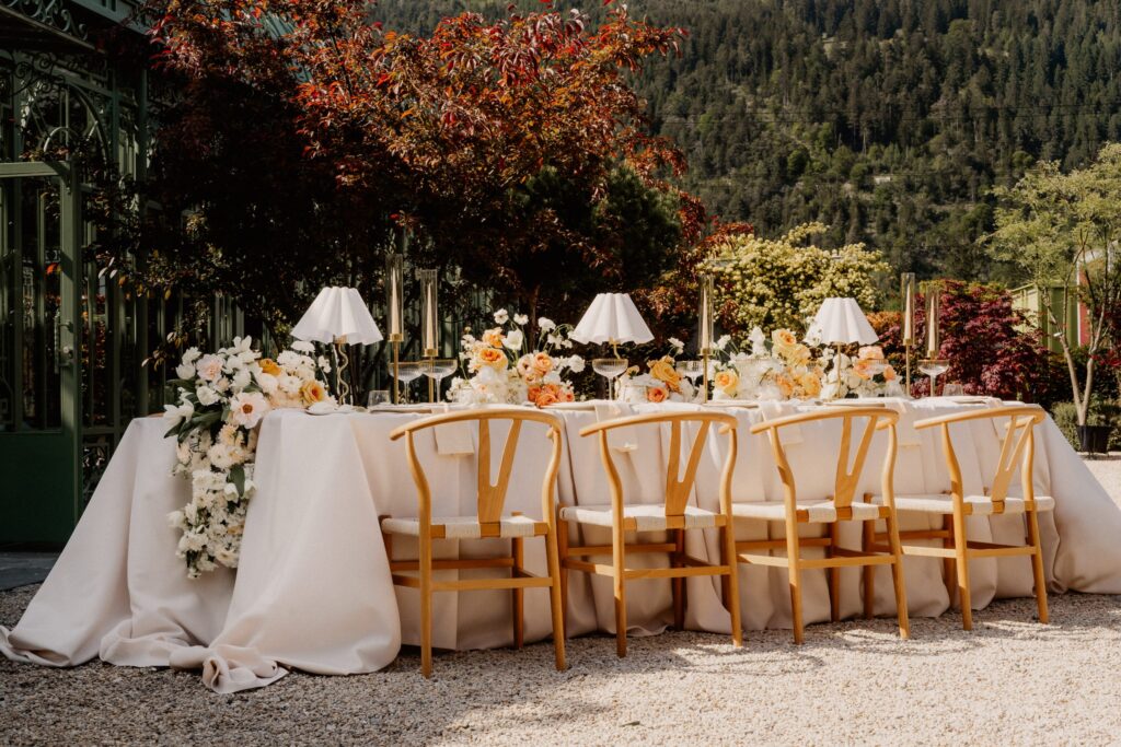 Lange Hochzeitstafel mit Lampen und Blumen in einem Garten vor Schweizer Bergkulisse