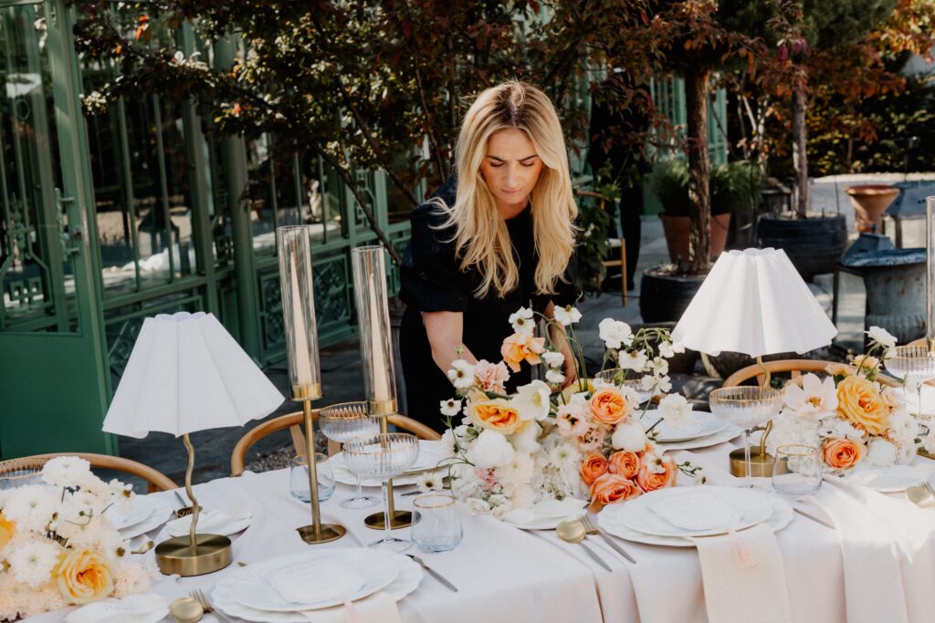 Wedding planner Selina Studenik is setting up a wedding table with lamps and peach-colored flowers in Switzerland