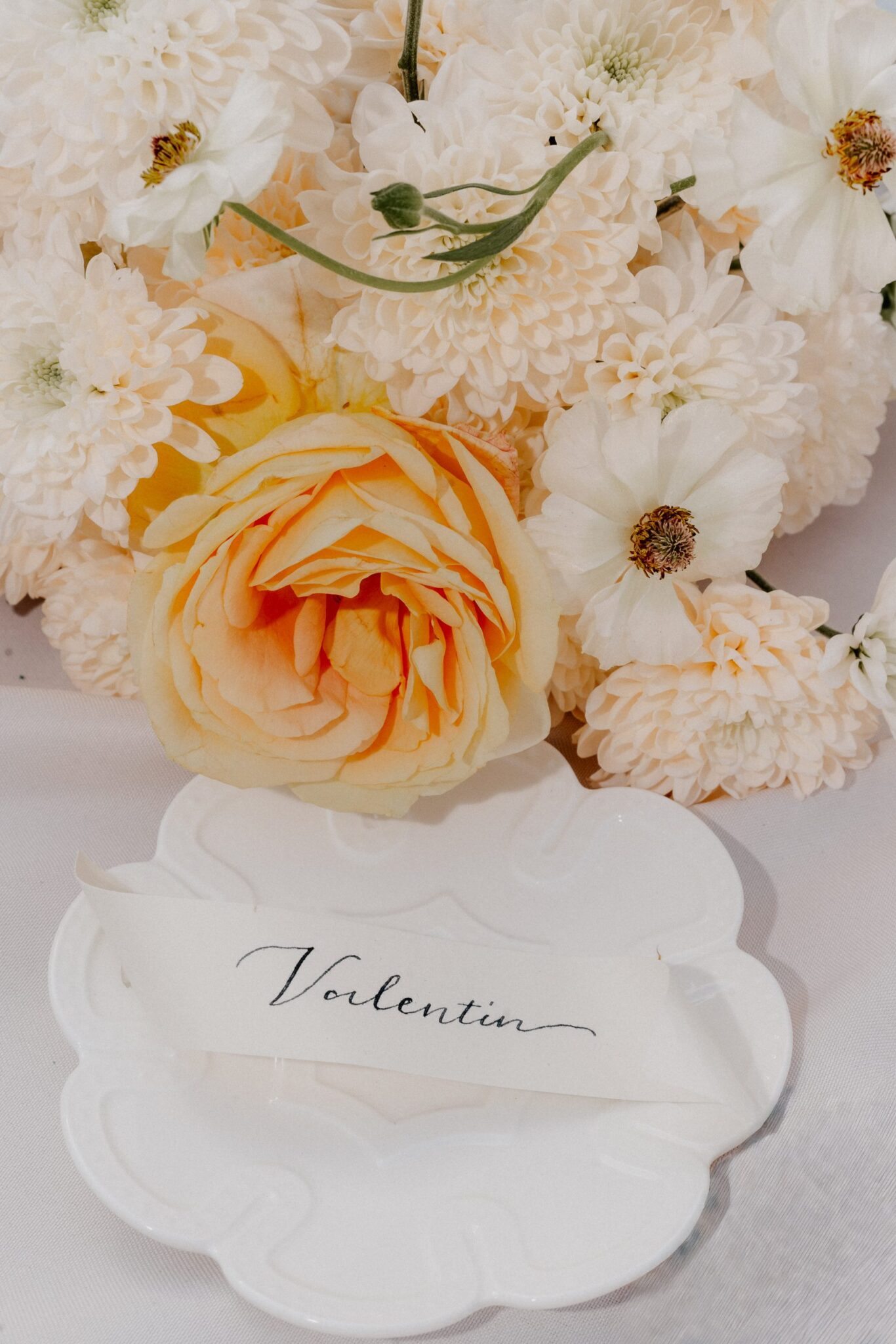 Hand-decorated table card between peach-colored roses and white flowers