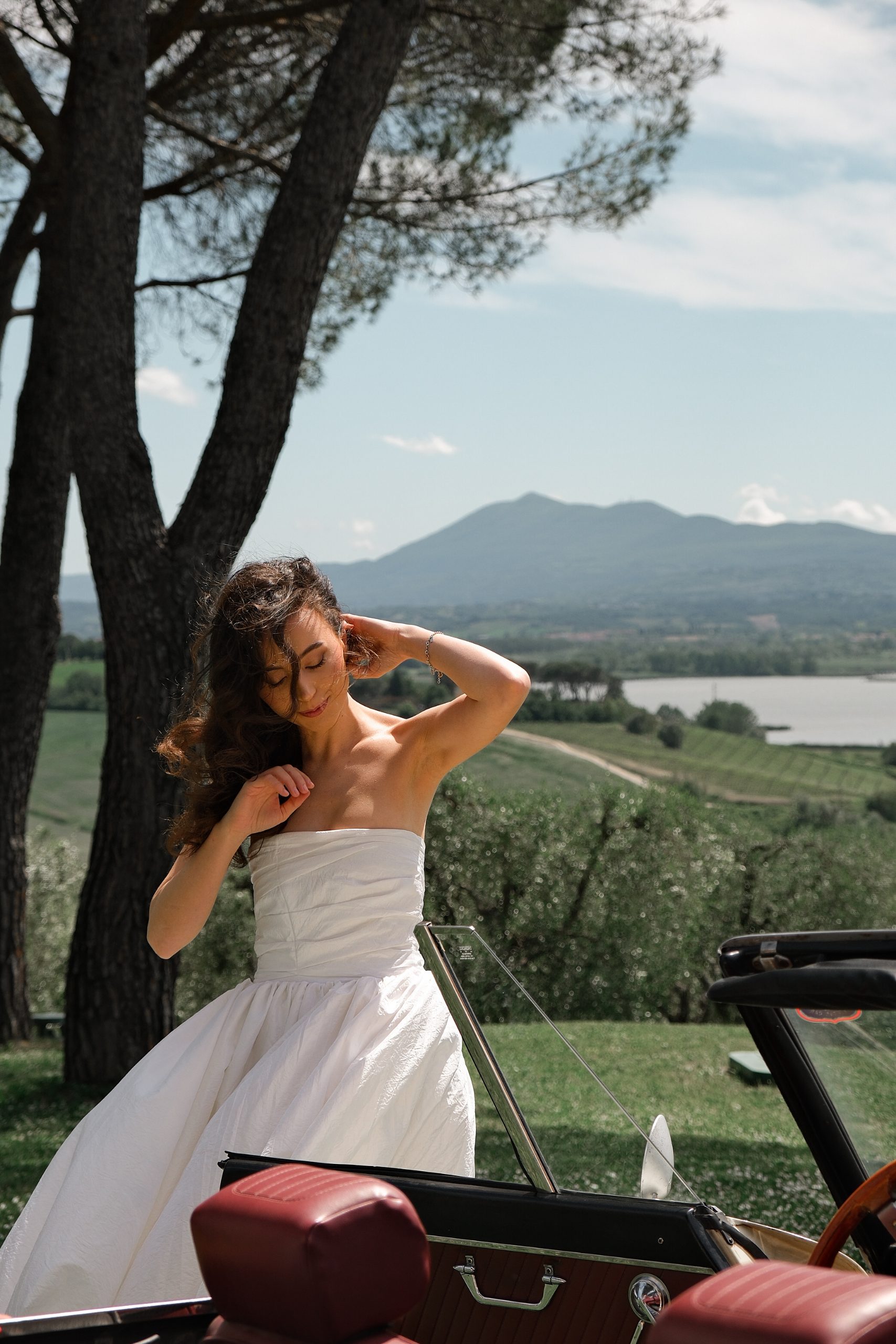 Bride posing in front of an old car under the pines in Tuscany